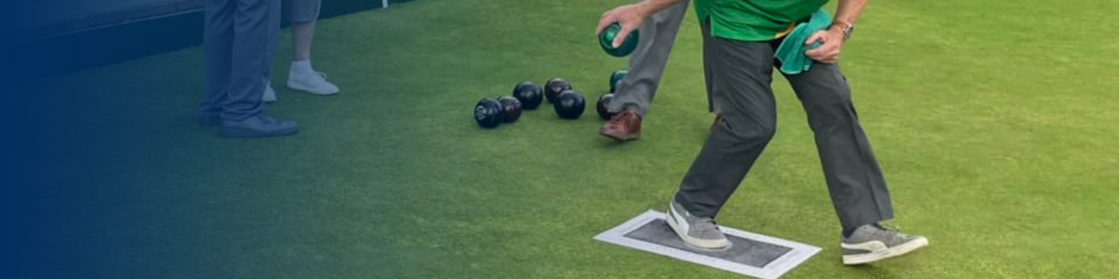 BOWLS - Image shows lawn bowls player holding the ball about to throw, there are several balls on the lawn behind them.